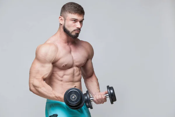 Muscular bodybuilder guy doing exercises with dumbbell over grey background — Stock Photo, Image