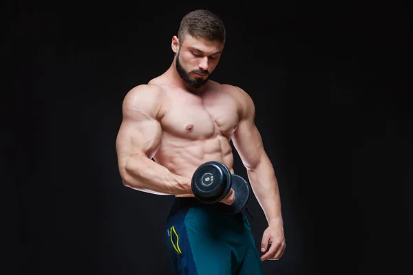 Muscular bodybuilder guy doing exercises with dumbbell over black background