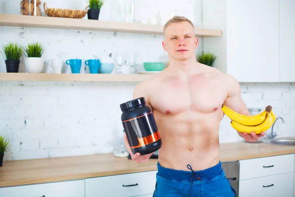 Svalnatý muž nahý trup v kuchyni s sportovní výživy proteiny a banány, koncept zdravé stravy. Sportovní způsob života. — Stock fotografie