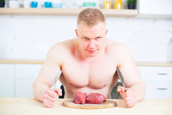 Homme musclé avec un torse nu dans la cuisine avec un morceau de viande de bœuf, le concept d'une alimentation saine. Mode de vie athlétique . — Photo