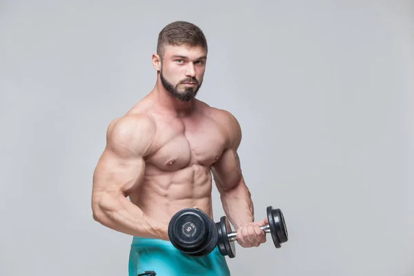 Muscular bodybuilder guy doing exercises with dumbbell over grey background — Stock Photo, Image