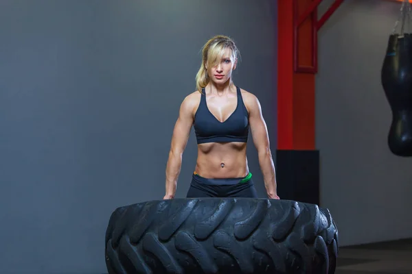 Apto atleta feminino exercitar-se com um pneu enorme, girando e transportar no ginásio. Crossfit mulher exercitando com pneu grande — Fotografia de Stock