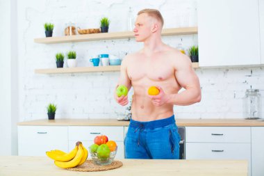 Kaslı adam meyve, sağlıklı beslenme kavramı ile mutfakta çıplak bir gövde ile. Atletik yaşam tarzının.