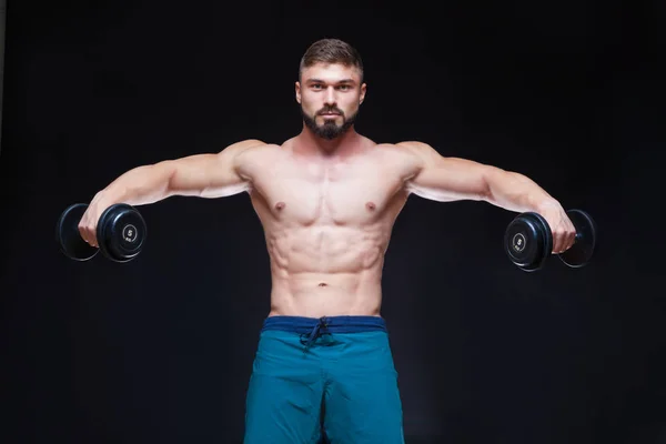 Gespierde bodybuilder man doen oefeningen met dumbbell op zwarte achtergrond — Stockfoto