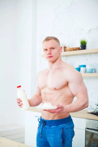 Uomo muscolare con un busto nudo in cucina con latte e ricotta, il concetto di una dieta sana. Stile di vita atletico . — Foto Stock
