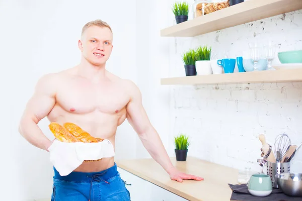 Homem musculoso com um tronco nu na cozinha com pão, conceito de alimentação saudável. Modo de vida atlético . — Fotografia de Stock