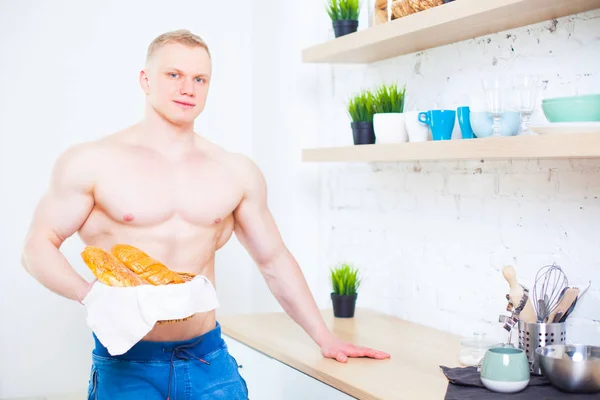 Homem musculoso com um tronco nu na cozinha com pão, conceito de alimentação saudável. Modo de vida atlético . — Fotografia de Stock