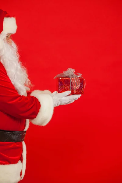 Foto de la mano enguantada de Santa Claus con caja de regalo, sobre un fondo rojo — Foto de Stock