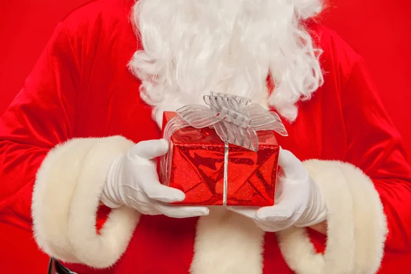 Photo of Santa Claus gloved hand with giftbox, on a red backgrou — Stock Photo, Image