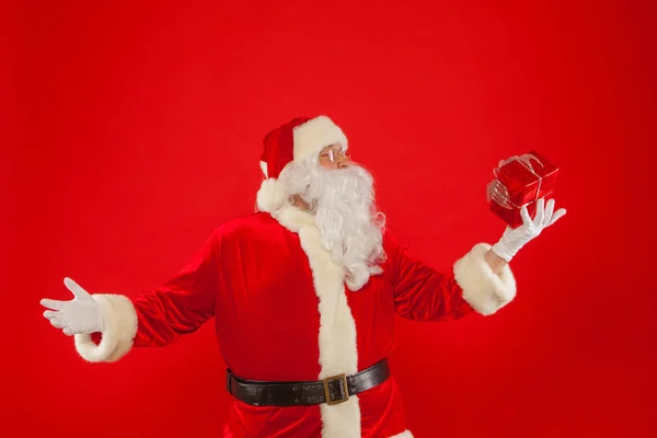 Foto de la mano enguantada de Santa Claus con caja de regalo, sobre un fondo rojo — Foto de Stock