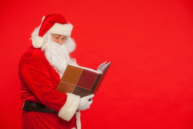 Noel Baba kırmızı bir arka plan üzerinde eski kitap okur. Noel