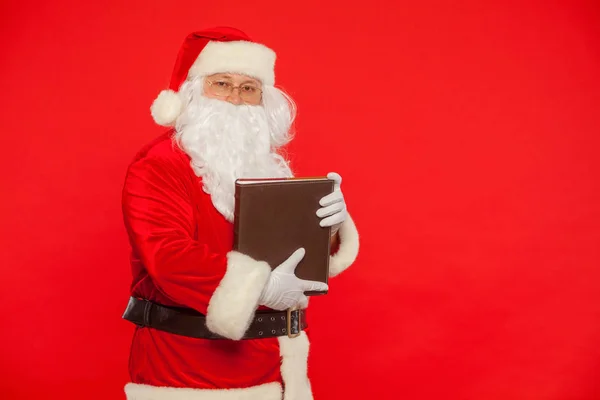 サンタ クロースは、赤い背景の上の古い本を読みます。クリスマス — ストック写真