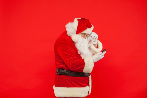 Foto de Santa Claus usando teléfono móvil, sobre un fondo rojo. Ch — Foto de Stock