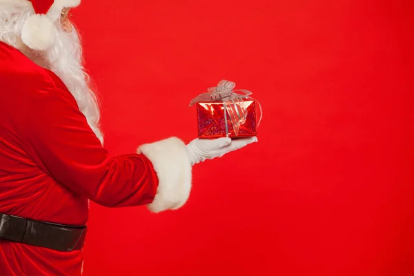 Foto der handschuhten Hand von Santa Claus mit Geschenkbox, auf rotem Hintergrund — Stockfoto
