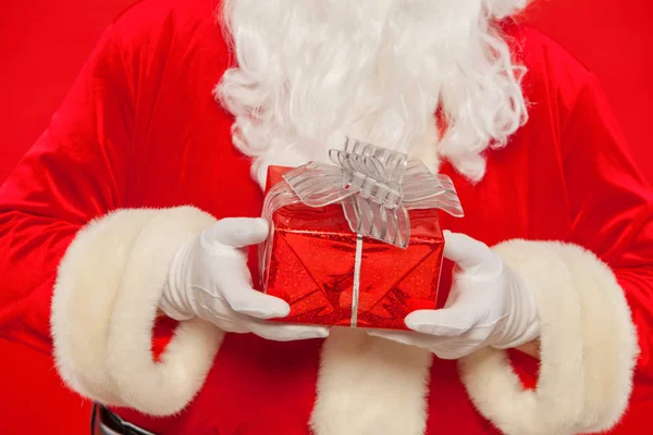 Foto de la mano enguantada de Santa Claus con caja de regalo, sobre un fondo rojo —  Fotos de Stock