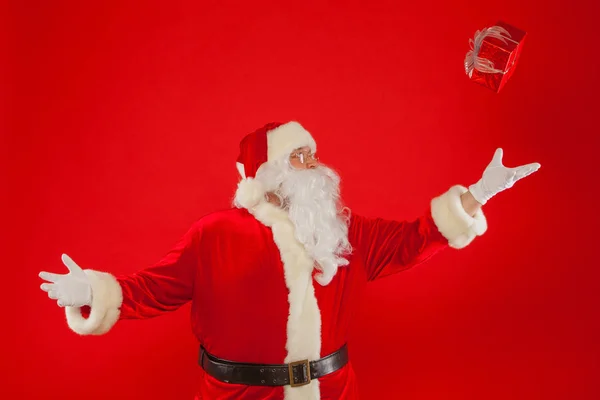 Foto de la mano enguantada de Santa Claus con caja de regalo, sobre un fondo rojo —  Fotos de Stock