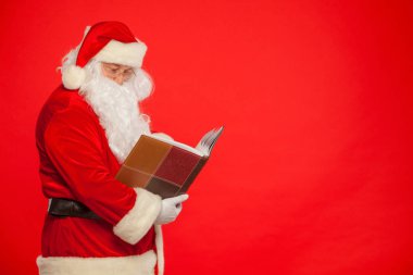 Noel Baba kırmızı bir arka plan üzerinde eski kitap okur. Noel