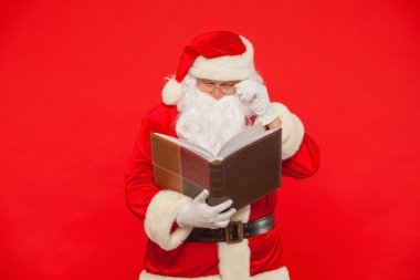 Noel Baba kırmızı bir arka plan üzerinde eski kitap okur. Noel