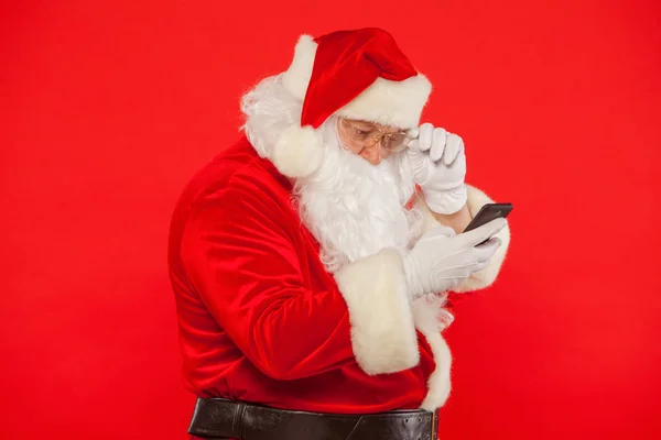 サンタ クロースの赤い背景の上の携帯電話を使用しての写真。Ch — ストック写真
