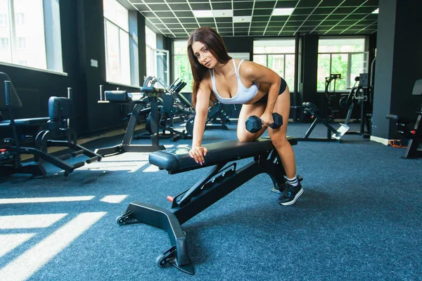 A girl performs a dumbbell with one hand in the slope using a bench. exercise on the broadest back muscles with dumbbells side view — Stock Photo, Image