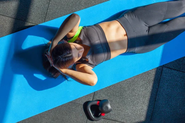 Fit young woman in sportwear lying on exercise mat near fitball and weight doing stomach exercises. Overhead view of female working out at the gym