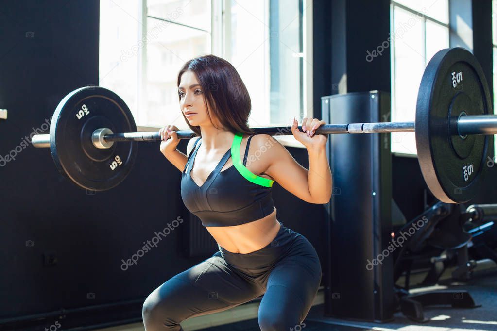 Young fit girl doing heavy duty squats in gym with barbell in beautiful sportswear