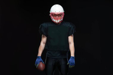 Kask ve holding topu siyah arka plan üzerinde siyah üniformalı Amerikan futbolu oyuncusu