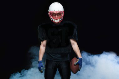 Siyah üniformalı, kask ve holding topu beyaz duman karşı Amerikan futbolu oyuncusu