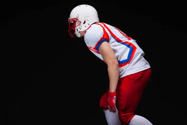 黒い背景と対戦しながらヘルメットの位置を取る身に着けてアメリカン フットボール プレイヤーの側面図 — ストック写真
