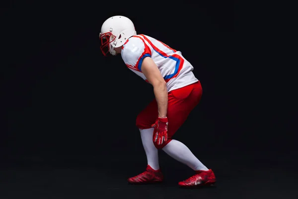 Vista lateral del jugador de fútbol americano que usa casco tomando posición mientras juega contra fondo negro — Foto de Stock