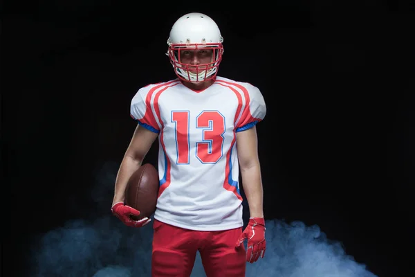 Retrato de vista frontal del jugador de fútbol americano que usa casco con pelota contra humo blanco — Foto de Stock