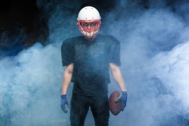 Siyah üniformalı, kask ve holding topu beyaz duman karşı Amerikan futbolu oyuncusu