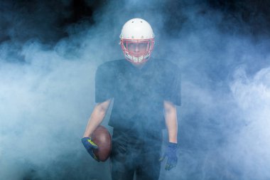Siyah üniformalı, kask ve holding topu beyaz duman karşı Amerikan futbolu oyuncusu