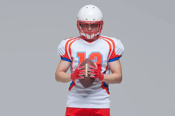 American football sportsman player wearing helmet holding rugby ball isolated on grey background — Stock Photo, Image