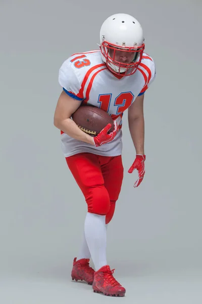 Aufnahme in voller Länge von American Football Sportler Spieler mit Helm posiert mit Rugby-Ball isoliert auf grauem Hintergrund — Stockfoto