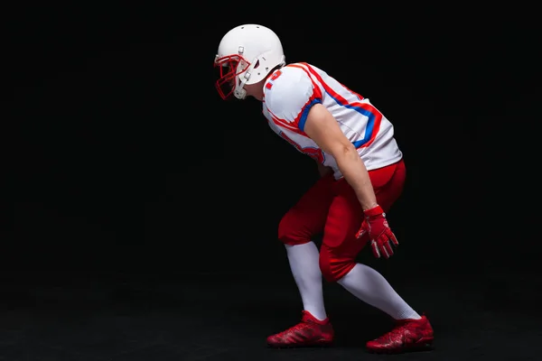 Vista lateral del jugador de fútbol americano que usa casco tomando posición mientras juega contra fondo negro — Foto de Stock