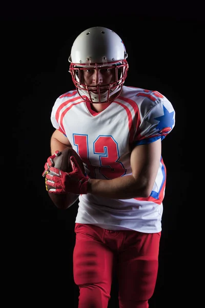 American football player wearing helmet ready to throw ball on black background