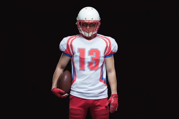 American Football-Spieler mit Helm posiert mit Ball auf schwarzem Hintergrund — Stockfoto