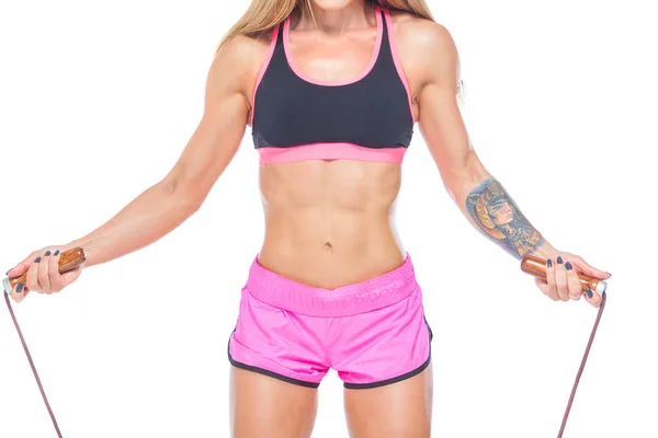 迷人的, 性感的, 肌肉发达的女孩在粉红色的短裤和黑色上衣跳过一个现代绳子与木制手柄。心脏训练。健身、健康生活方式的理念。隔离在白色背景上. — 图库照片