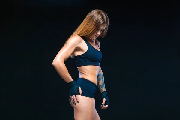 Black boxing bandages on the hands of a muscular girl in black clothes. Boxing, kickboxing, karate. Fitness, healthy lifestyle concept. Isolated on the black background.