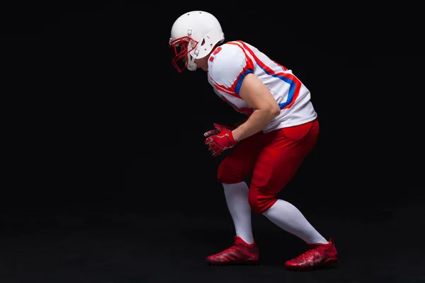 Vista lateral del jugador de fútbol americano que usa casco tomando posición mientras juega contra fondo negro — Foto de Stock