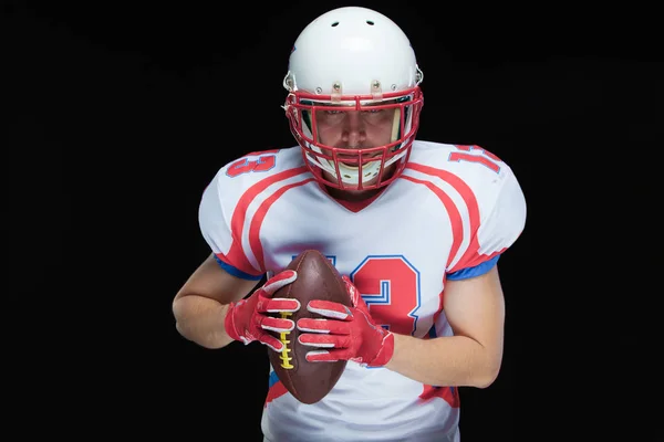 American Football-Spieler mit Helm posiert mit Ball auf schwarzem Hintergrund — Stockfoto