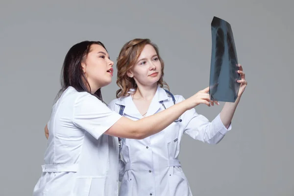 Две молодые женщины-доктора изучают рентгеновские снимки легких на сером фоне — стоковое фото
