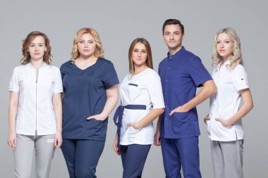 Tıbbi doktorlar başarılı takım gri arka planda ayakta iken kamera bakıyor