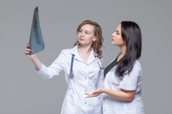 Две молодые женщины-доктора смотрят на рентгеновские снимки легких на сером фоне — стоковое фото