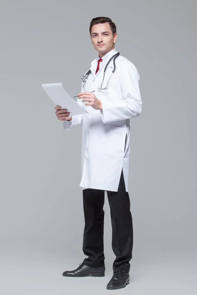 Teljes hosszúságú portréja fiatal orvos fehér egyenruhát sztetoszkópos Holding mappa — Stock Fotó