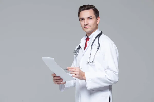รูปภาพของหมอหนุ่มในชุดยูนิฟอร์มสีขาวที่มีโฟลเดอร์การถือสเตโตสโกป — ภาพถ่ายสต็อก