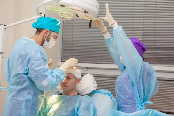 O cirurgião dirige a luz da lâmpada. Tratamento da calvície. Transplante de cabelo. Cirurgiões na sala de cirurgia realizar cirurgia de transplante de cabelo. Técnica cirúrgica que move os folículos pilosos de uma parte de — Fotografia de Stock