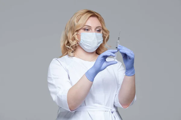 Female doctor in face mask holding syringe. Portrait of young woman doctor or nurse in protective gloves holding an injection