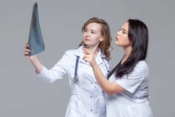 Dos doctoras jóvenes estudiando la radiografía de los pulmones sobre fondo gris — Foto de Stock